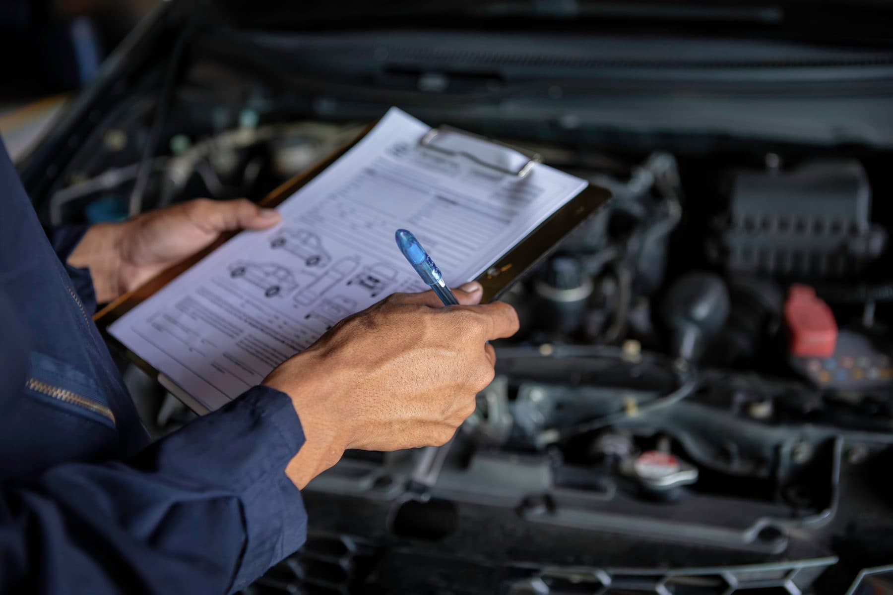A technician filling in a vehicle inspection checklist over an open engine bay