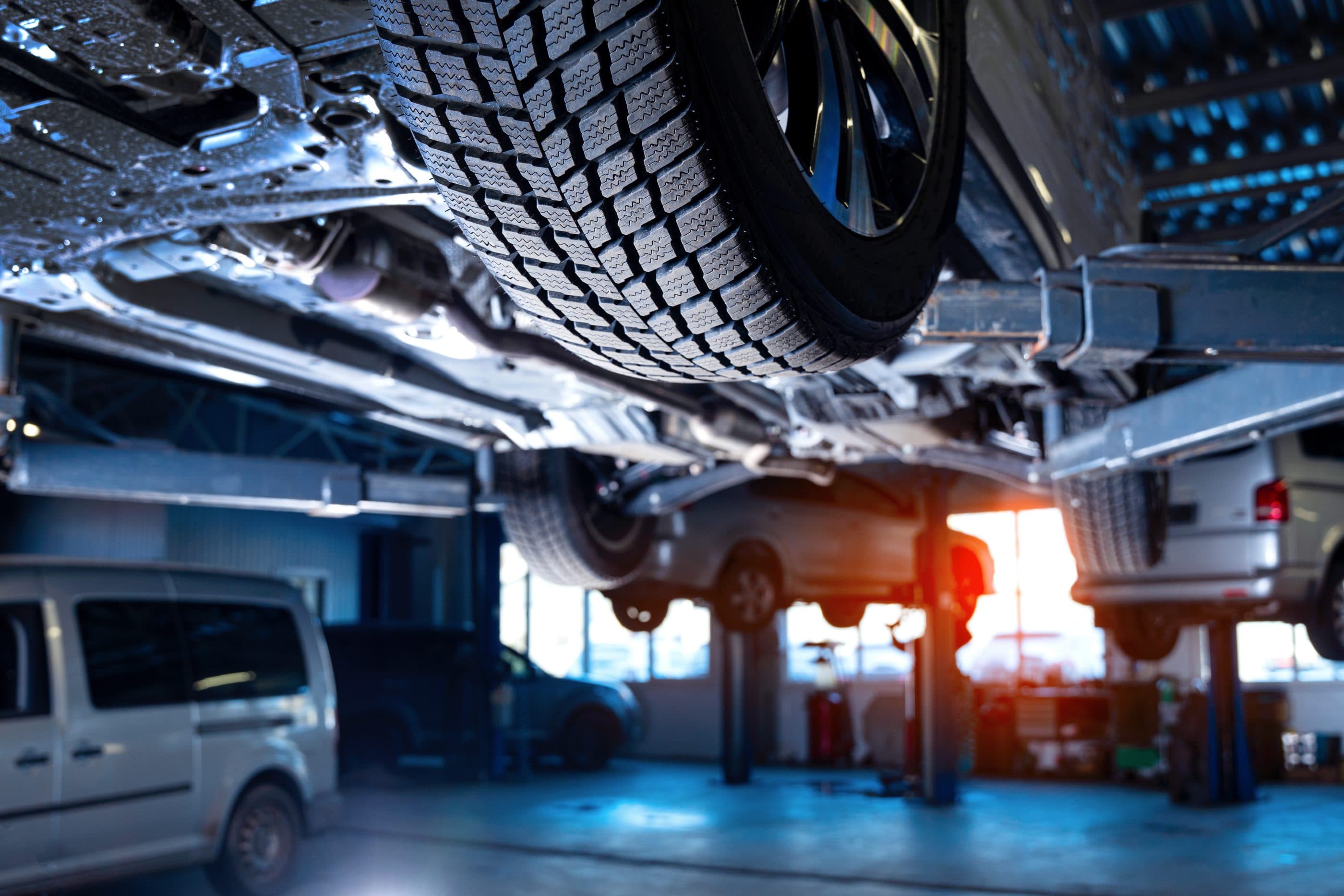 Looking up at a car raised on a lift in a modern MOT workshop, with more cars on lifts behind