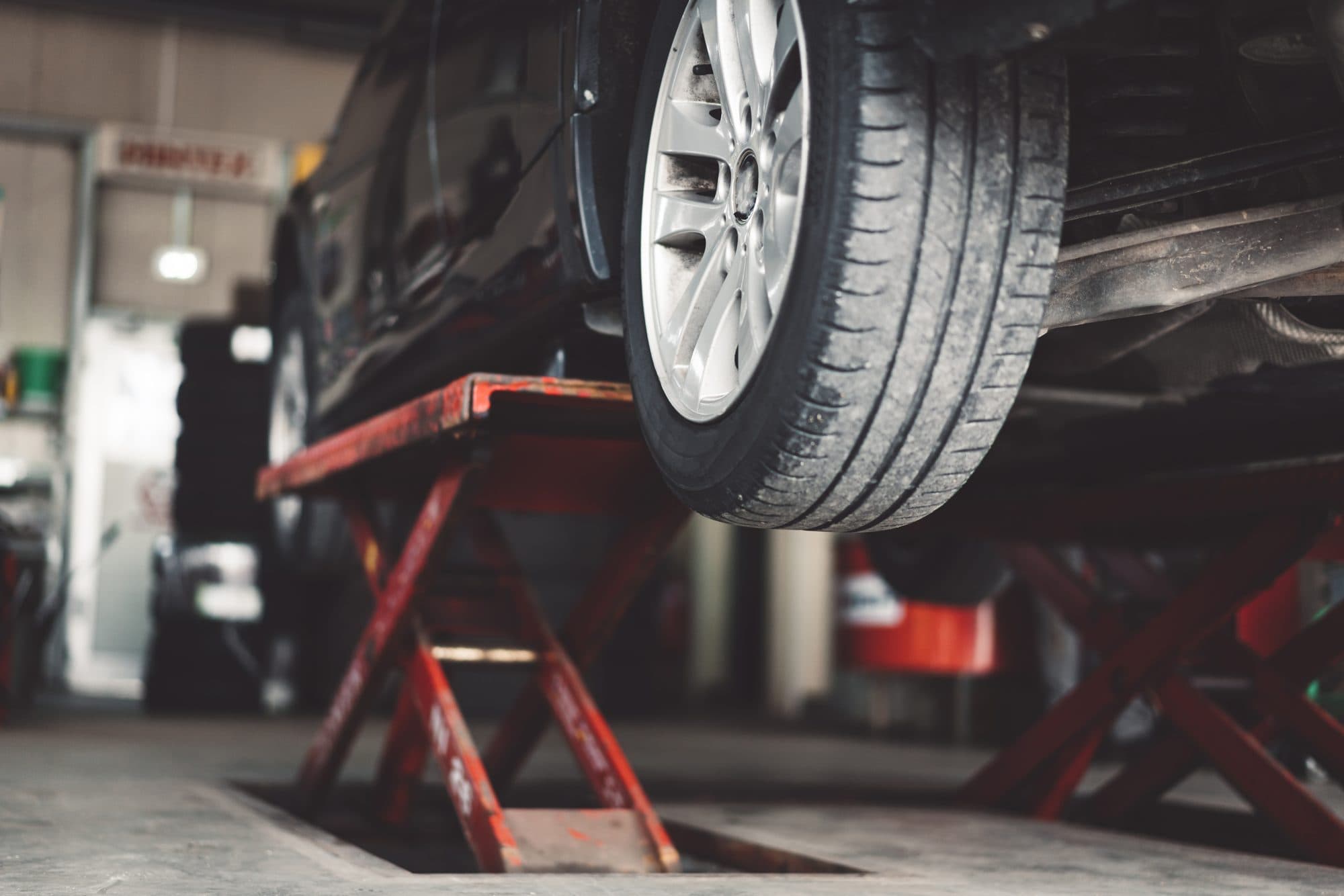 A car raised on a scissor lift over an inspection pit in an MOT bay